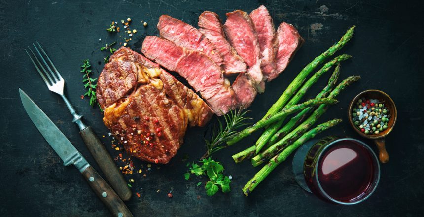 Roasted rib eye steak with green asparagus and wine on dark background